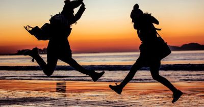 Two girls jumping on the beach at sunset