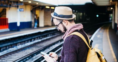 Man scrolling on his phone on a train platform