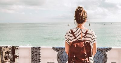 woman in black and white striped shirt with bun and red backpack looking at ocean