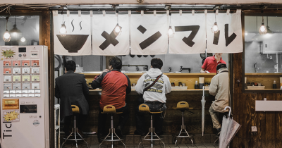 backs of men sitting at ramen bar in Taito, Japan