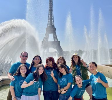 Group of teenage girls posing and smiling in front of the Eiffel Tower