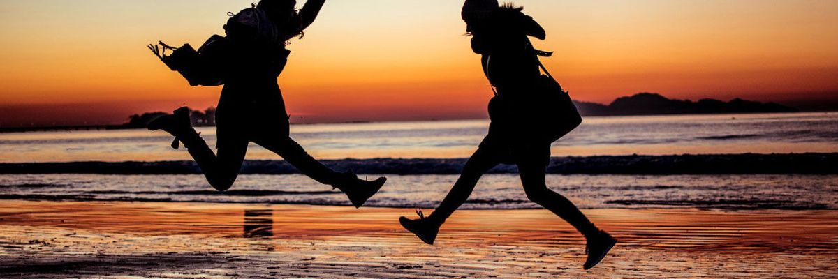 Two girls jumping on the beach at sunset