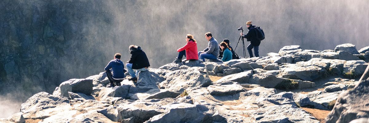 Group of adventurers resting on rocks, admiring and photographing the beauty of a mountain mist
