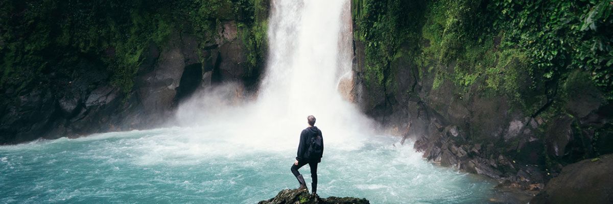 Man standing on edge of rock looking at waterfall
