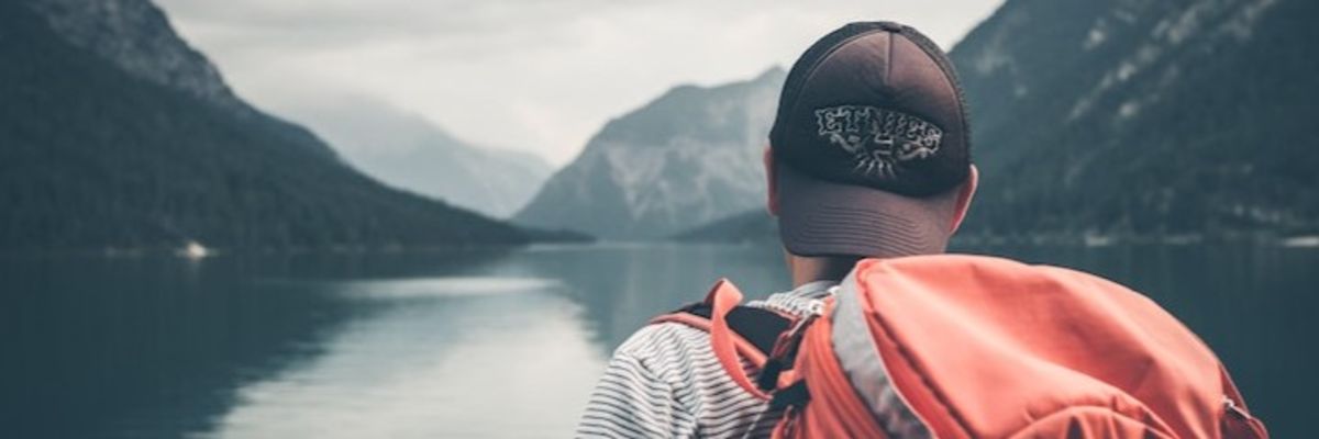 back of person wearing a backpack as they look out on water and mountains