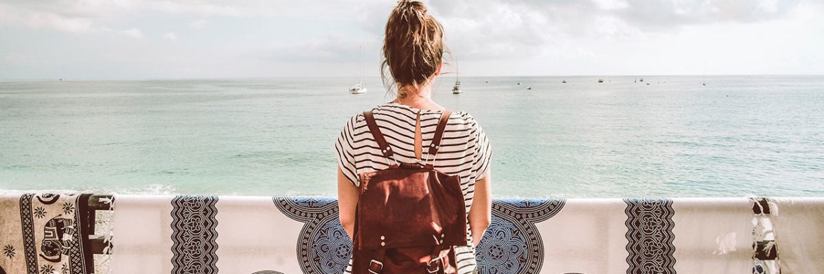 woman in black and white striped shirt with bun and red backpack looking at ocean