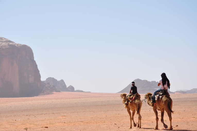 two people on camels on sand