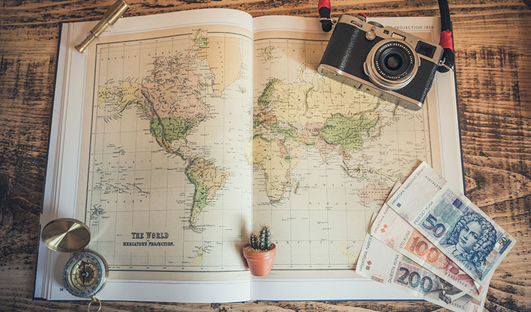 Flat lay photography of a world map, money, compass, cactus and a tiny telescope model.
