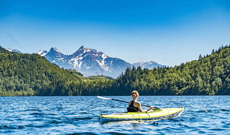 woman kayaking in mountain lake surrounded by forest