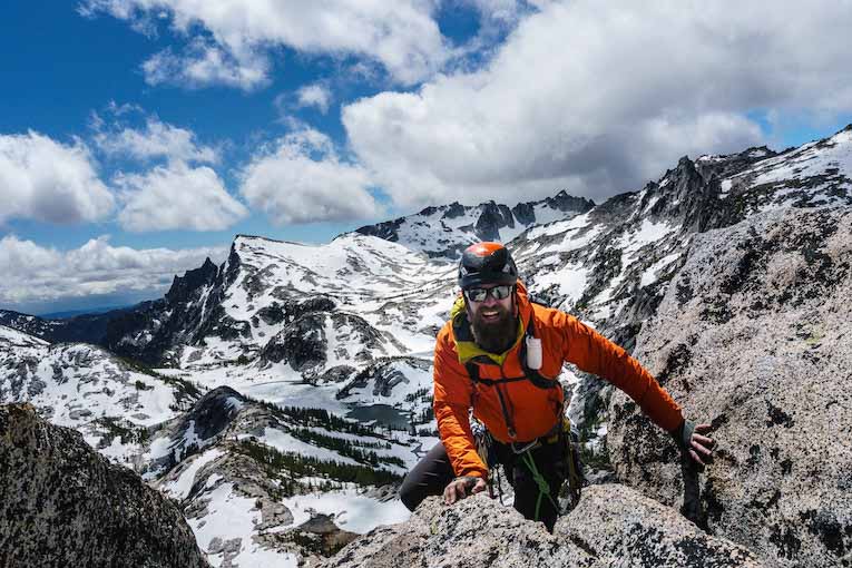 a smiling person climbing a rugged mountain in hiking gear