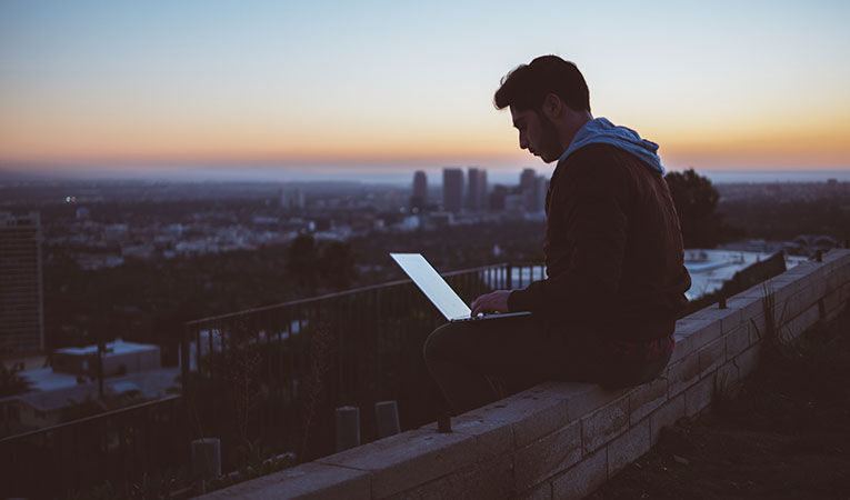 man working on laptop at sunrise on ledge
