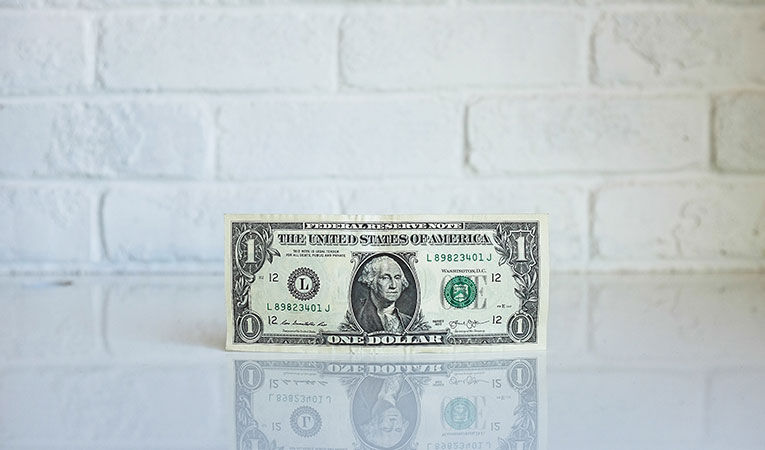 A one dollar bill leaning against the wall on a glossy surface