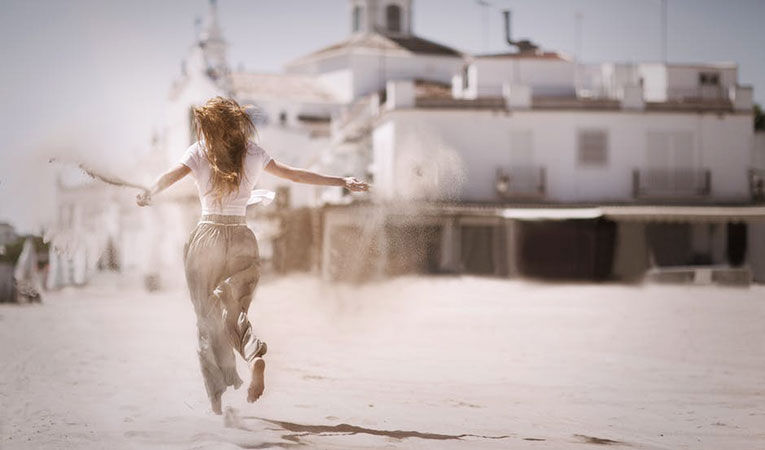 woman running on sand near white concrete building