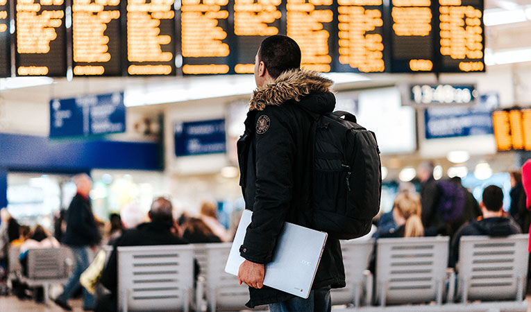 person with parka and backpack looking at departures board