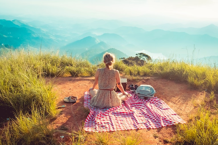 person sitting on picnic blanket overlooking mountains