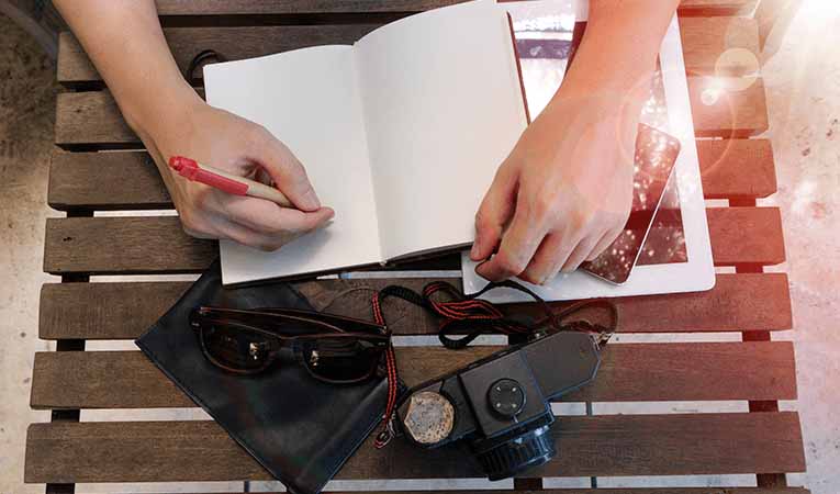 Writing in journal with film camera and smartphone out on table