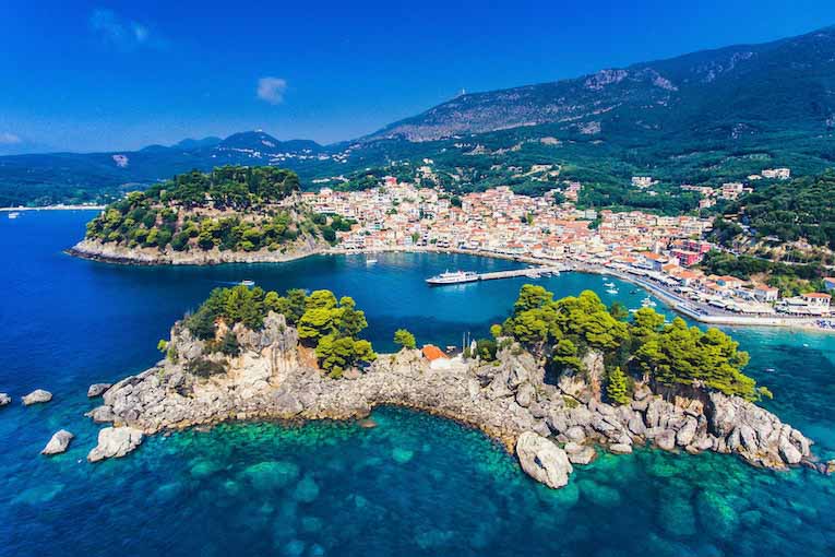 A seaside village in Greece is surrounded by lush green trees.