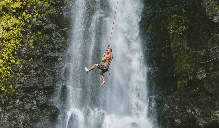 Man on rope swing into a waterfall
