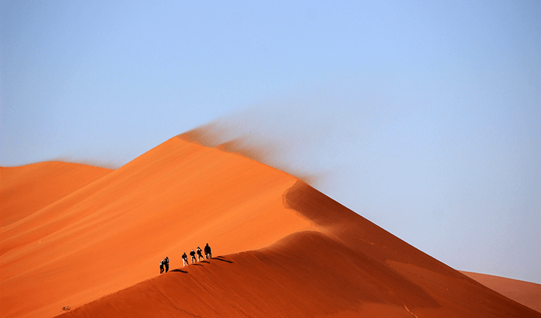 Group hiking up sand dunes