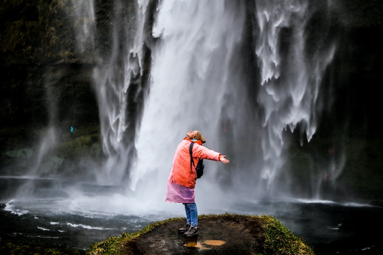 person with arms outstretched standing in front of waterfall