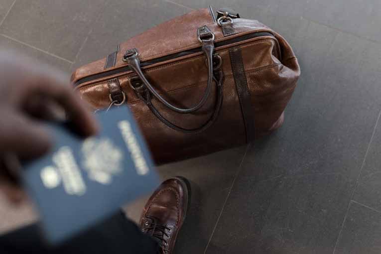 A leather duffle bag on the ground with an American passport out of focus