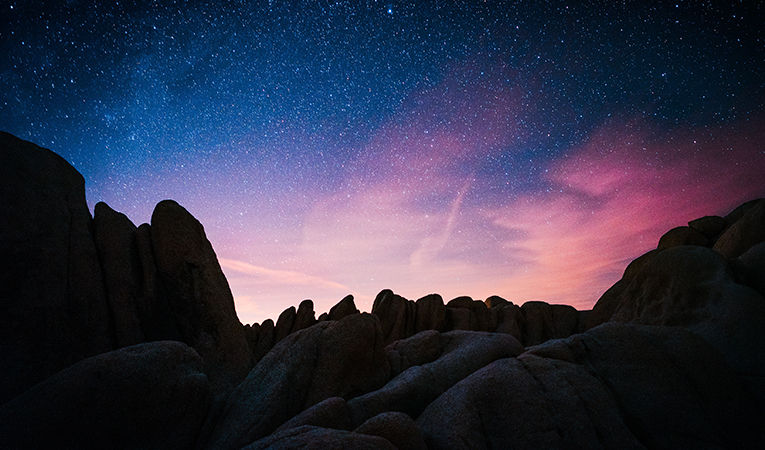 sunset over boulder field with bright stars fading into the night sky