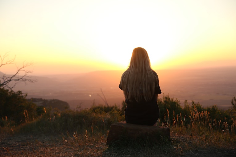 person sitting on a rock overlooking a valley at sunset