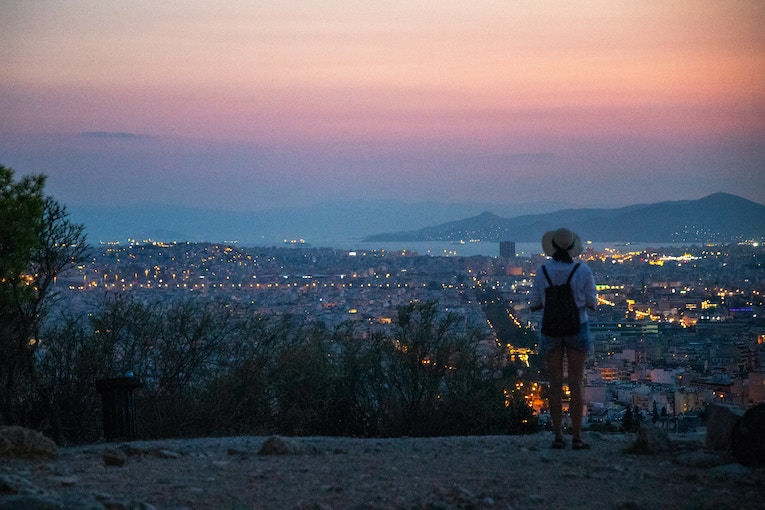 study abroad student standing on a hilltop overlooking athens at sunset