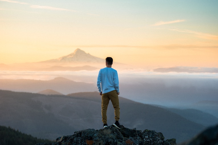 solo traveler standing on a mountain peak with white capped mountains in the distance