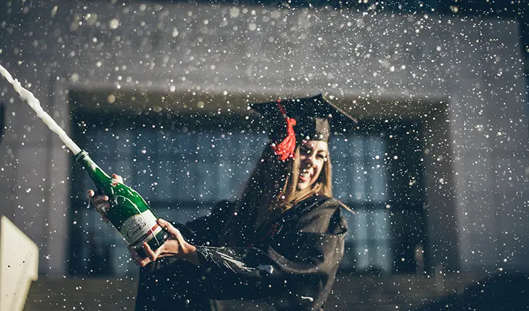 girl in graduation gown and red tassel popping champagne