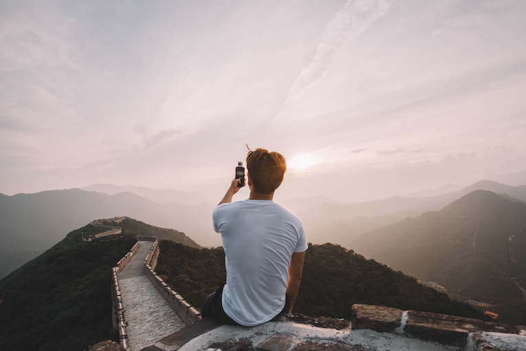 person on cliff at Great Wall of China taking photo with phone