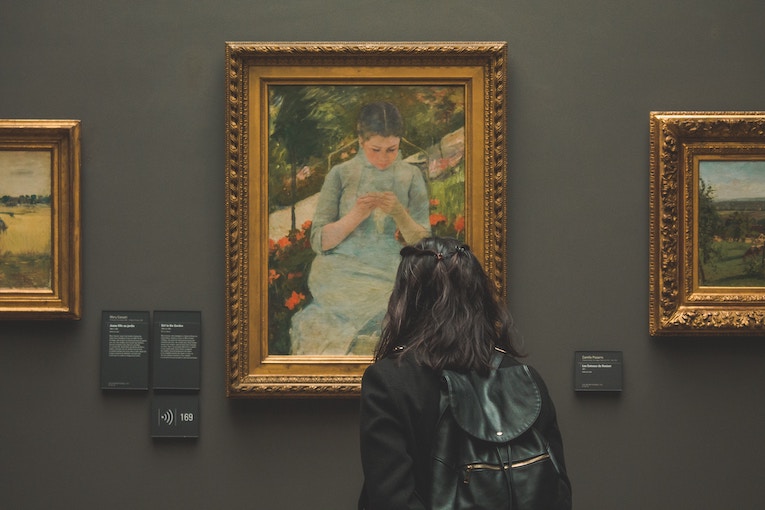 back of person looking at framed painting in a museum