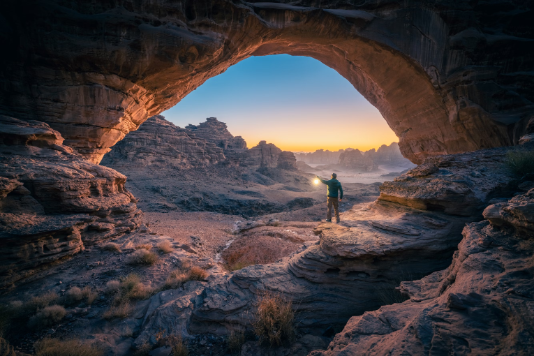 person standing in cave holding light at sunset