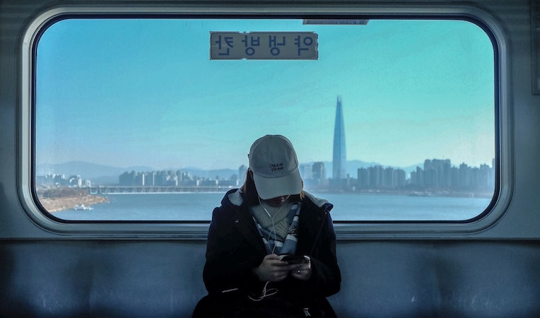 person looking at their phone on a train with seoul skyline in the background