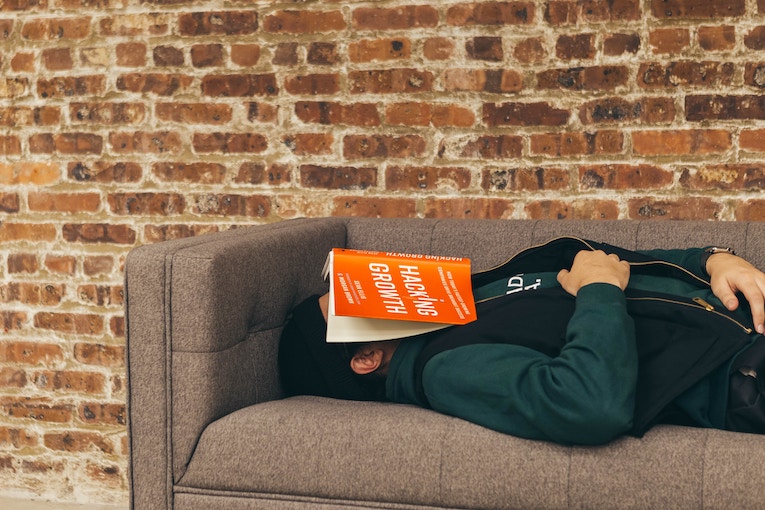 person lying on sofa with book covering face