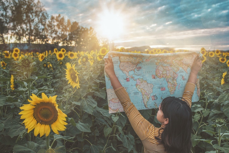person standing in field of sunflowers holding up world map