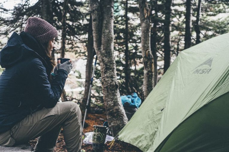 person sitting by a camp sight drinking from a cup