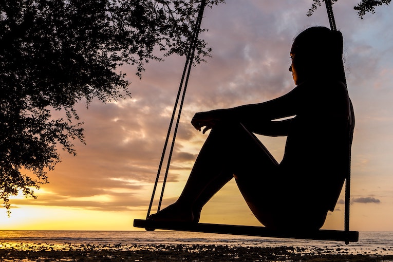 person sitting alone on a swing, silhouetted by the sunset