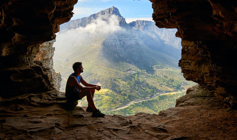 traveler sitting in cave silhouette by panoramic mountain views