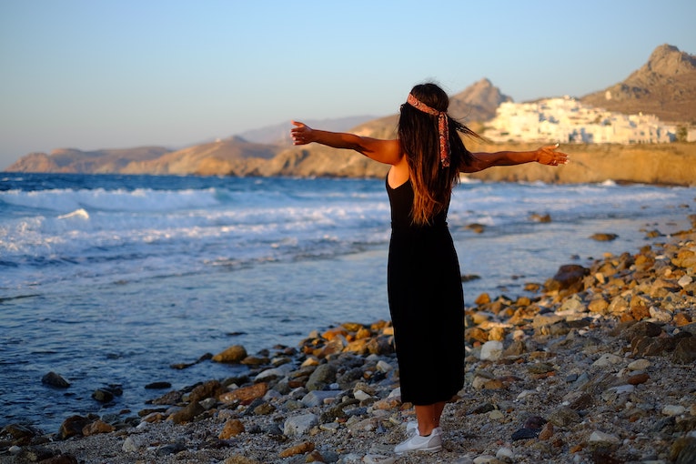 study abroad student in greece standing on a beach with arms outstretched and open