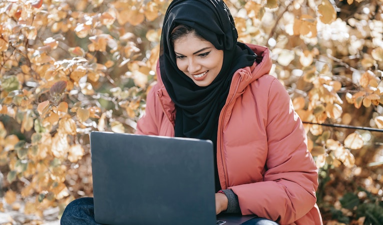 A smiling person uses a laptop in an autumn garden