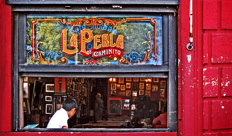 La perla de caminito - red storefront and window with man sitting at table
