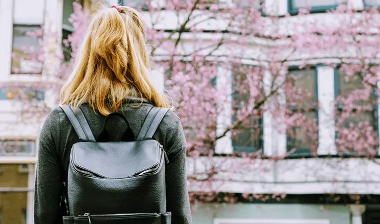 Blond woman with black leather backpack standing in front of row houses