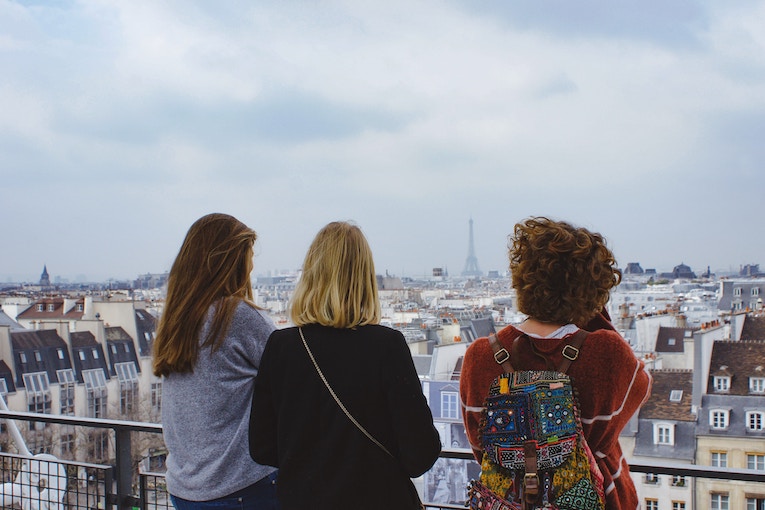 backs of three people in focus as they look out toward Eiffel Tower in the distance
