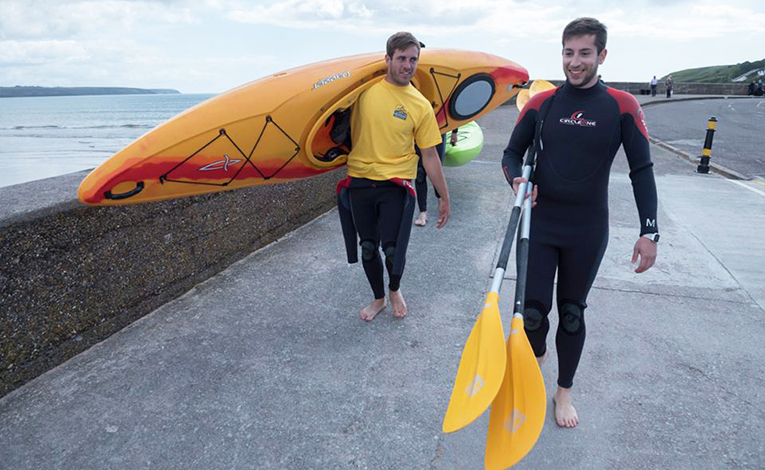 two guys carrying kayak and paddles