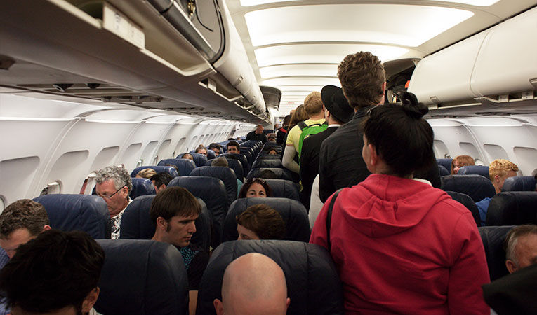 airplane passengers filing down the airplane aisle while boarding