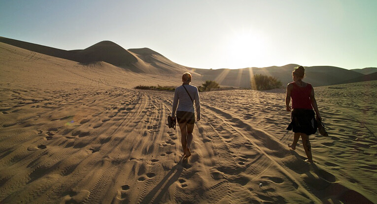 two people walking barefoot in sand dunes