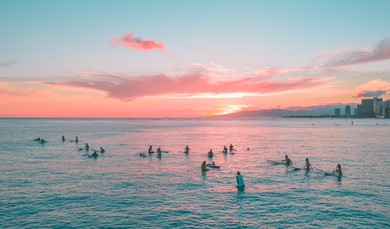 people on surf boards in the ocean at sunset