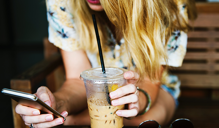 blond girl with iced coffee on her smartphone
