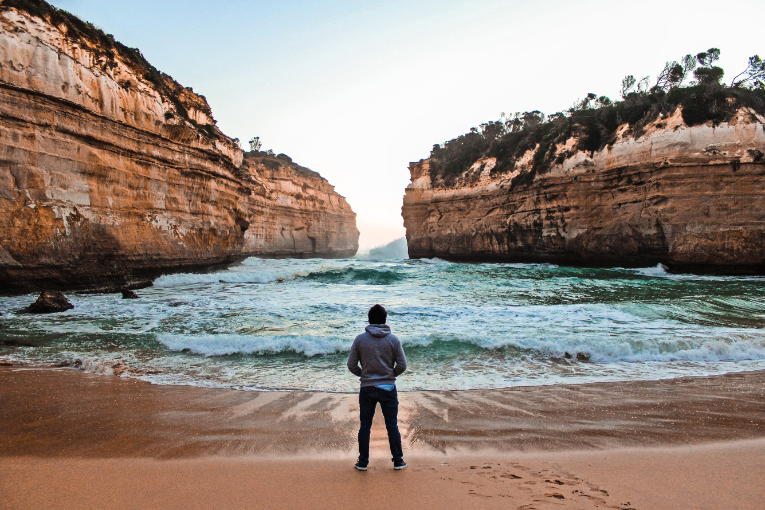 person standing on beach and looking out at water at twelve apostles, australia